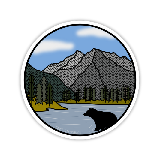 Round sticker with a bear, mountain, and lake illustration on a white background
