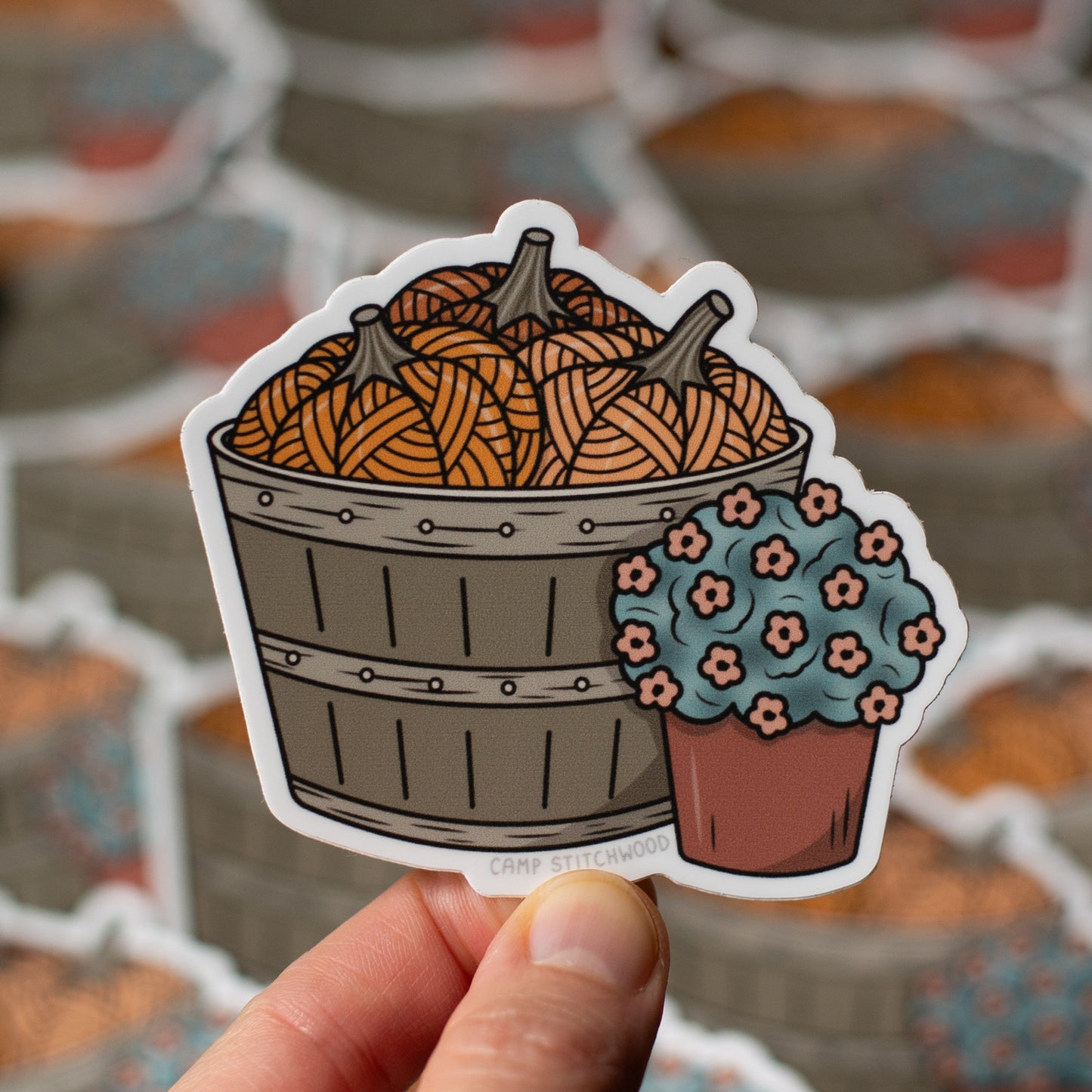 Sticker of a basket with pumpkins and a flower pot held in front of a blurred background.