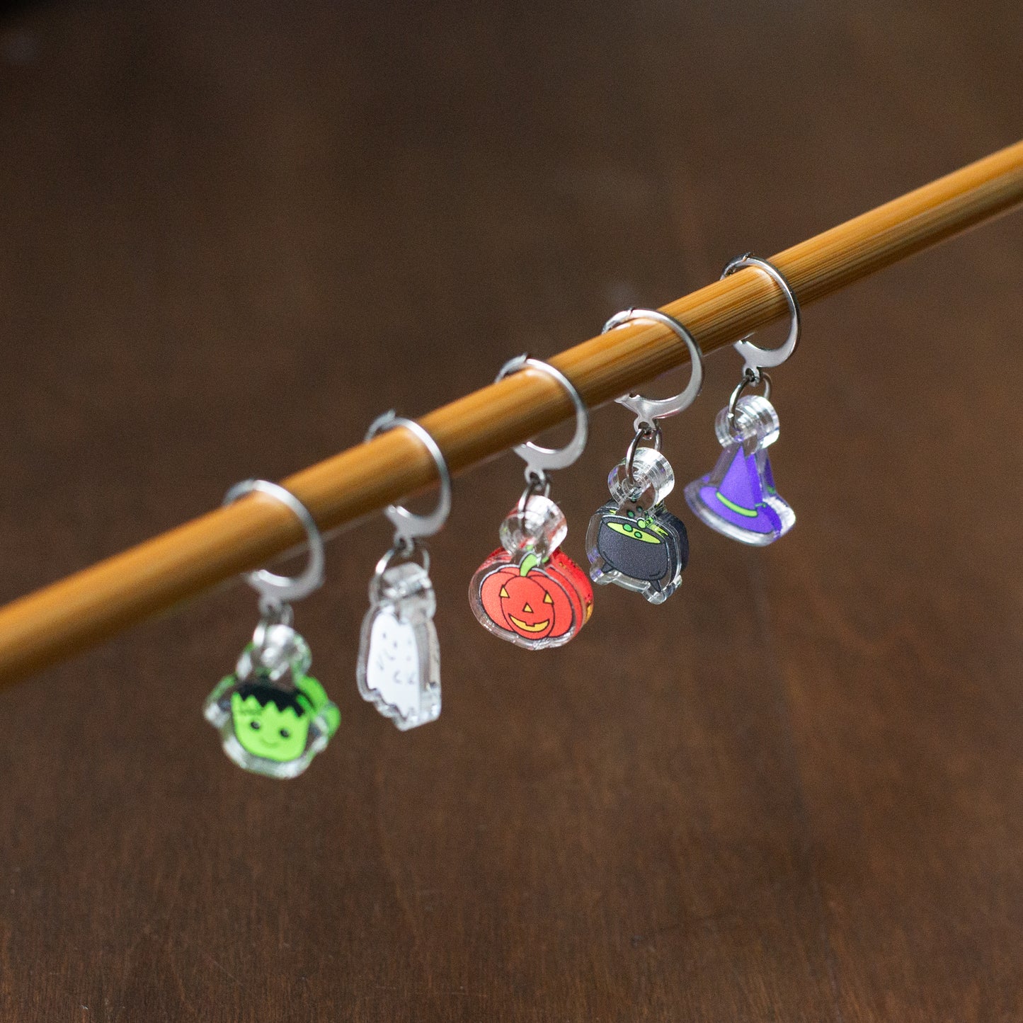 A set of Halloween stitch markers hanging from a knitting needle