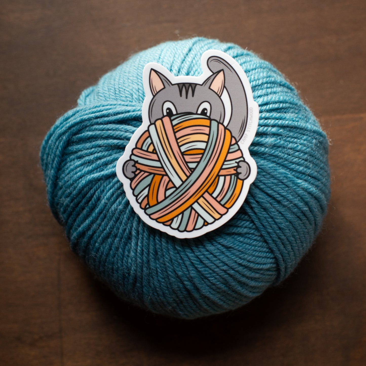 Blue yarn ball with a sticker of a cat playing with yarn on a wooden background