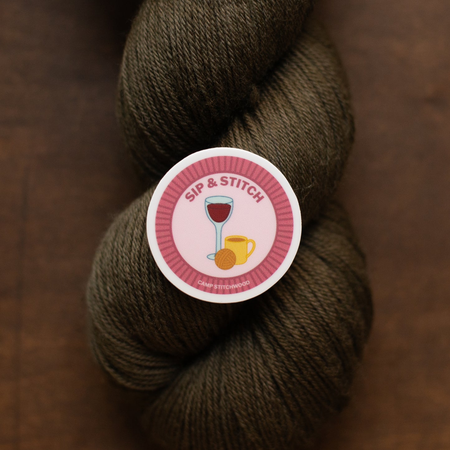 Brown skein of yarn with a 'Sip & Stitch' label on a brown background