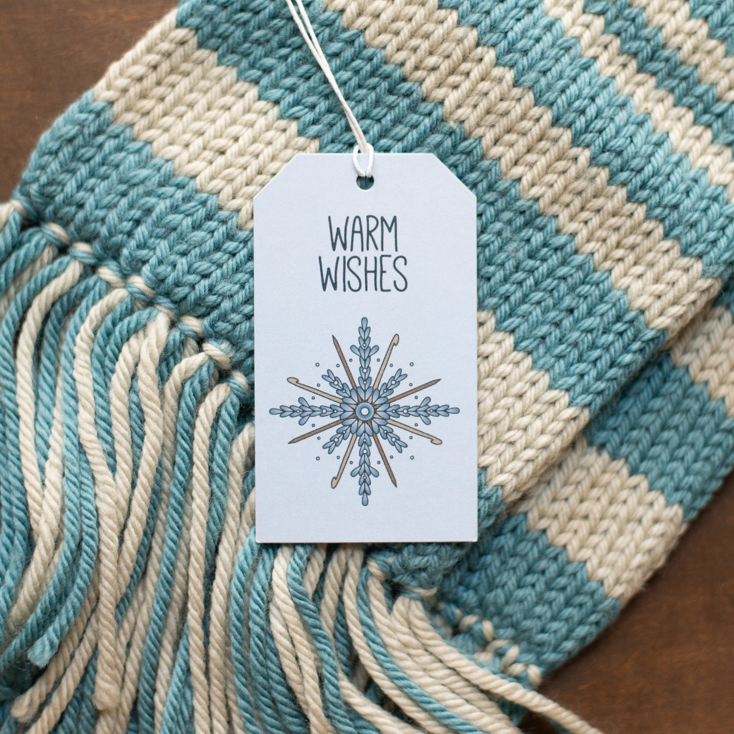 Knitted scarf with a 'Warm Wishes' tag featuring a snowflake design.
