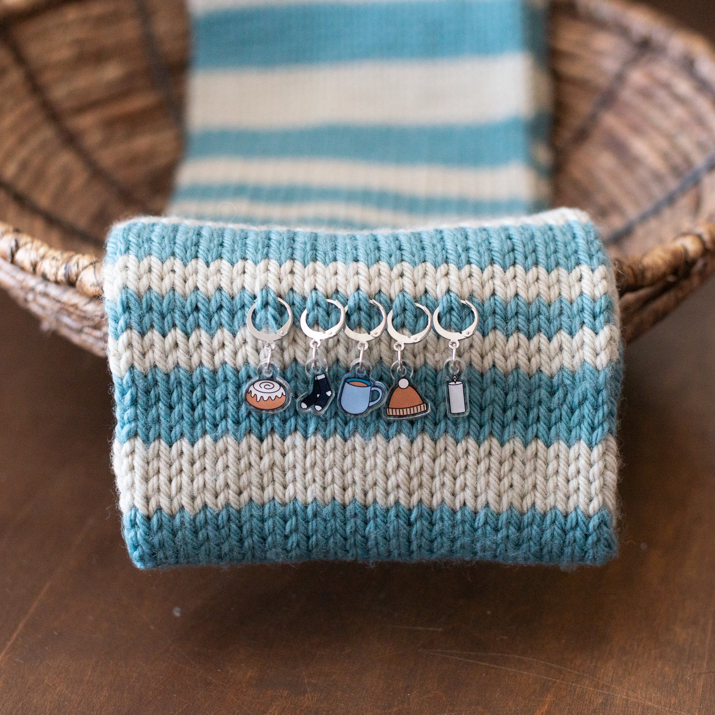 Knitted scarf with blue and white stripes and decorative stitch markers on a wooden surface.