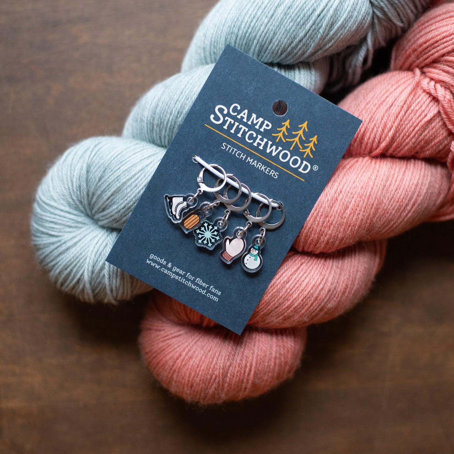 Yarn skeins with Camp Stitchwood stitch markers on a brown background