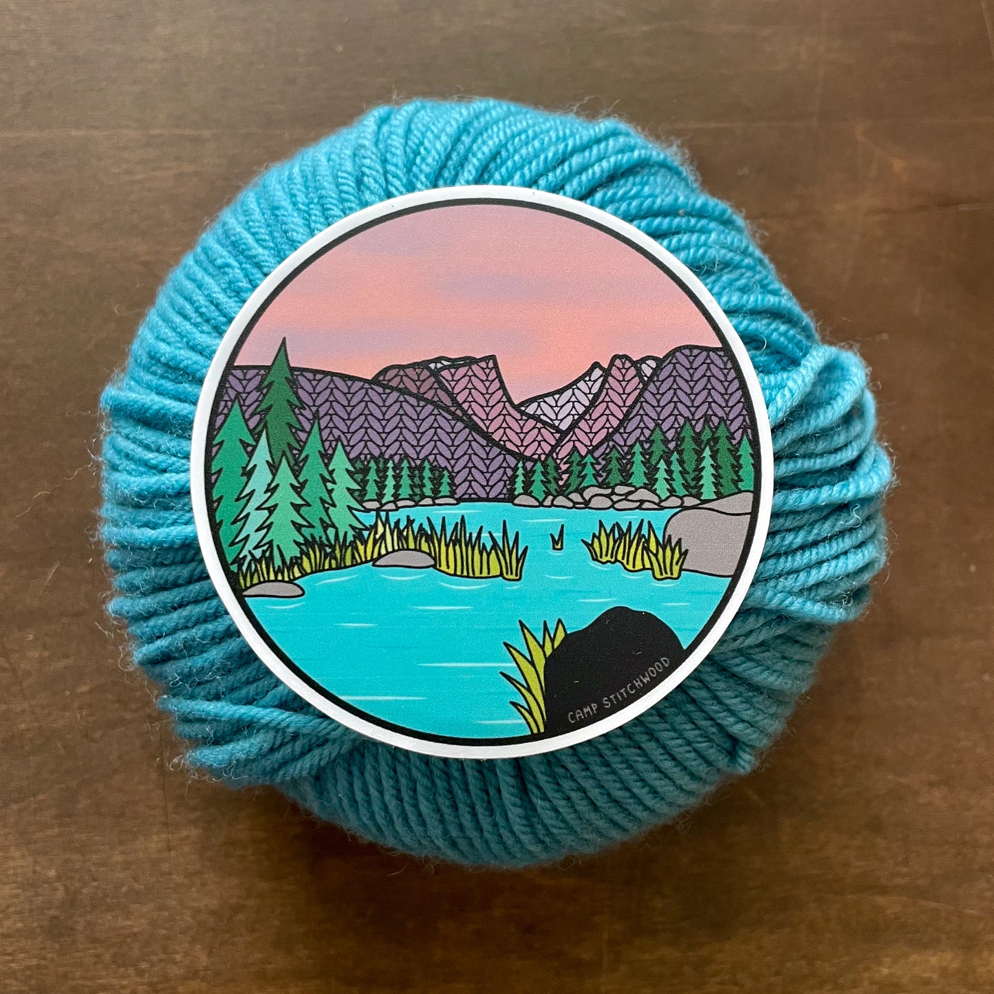 Blue yarn ball with a scenic sticker on a brown surface