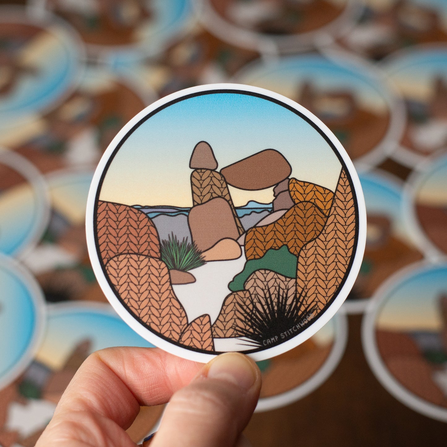 Sticker of a desert landscape held by a hand with more stickers in the background