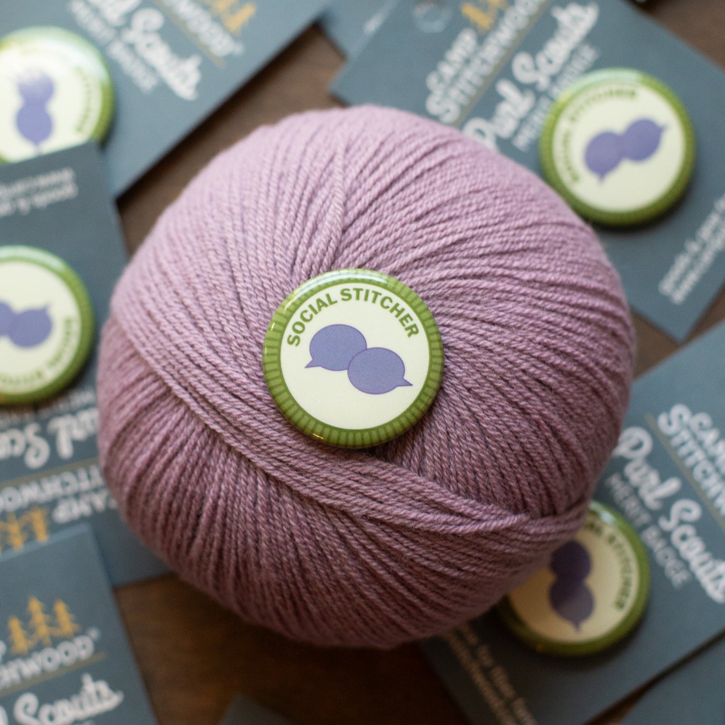 Ball of pink yarn with a 'Social Stitcher' label on a wooden surface with brochures.
