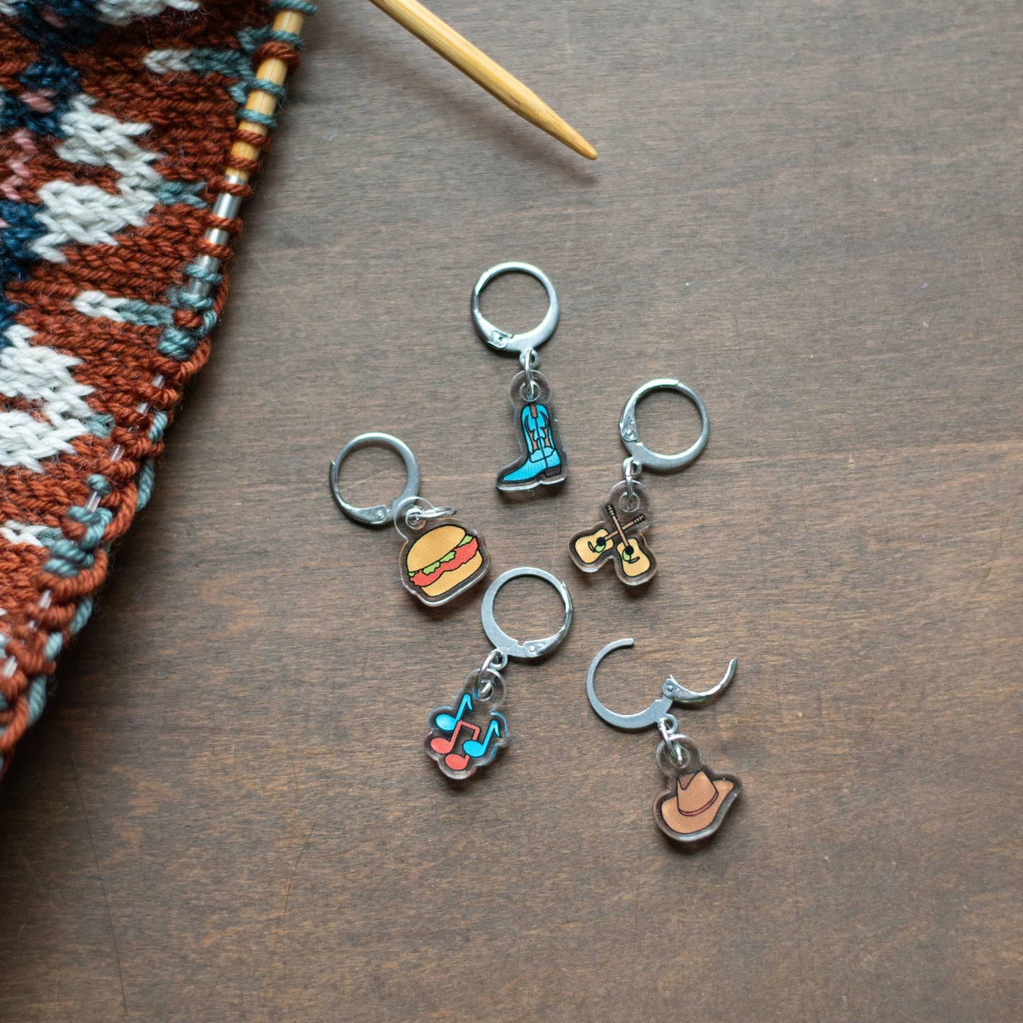 Set of colorful stitch markers on a wooden surface with knitting materials.