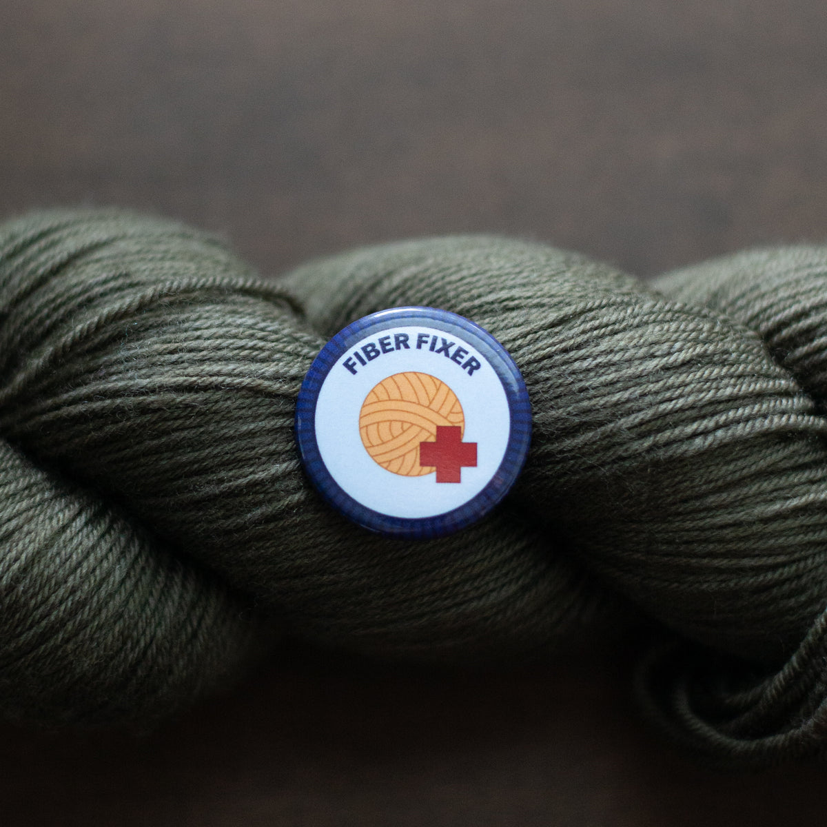 a fiber fixer badge on dark green yarn