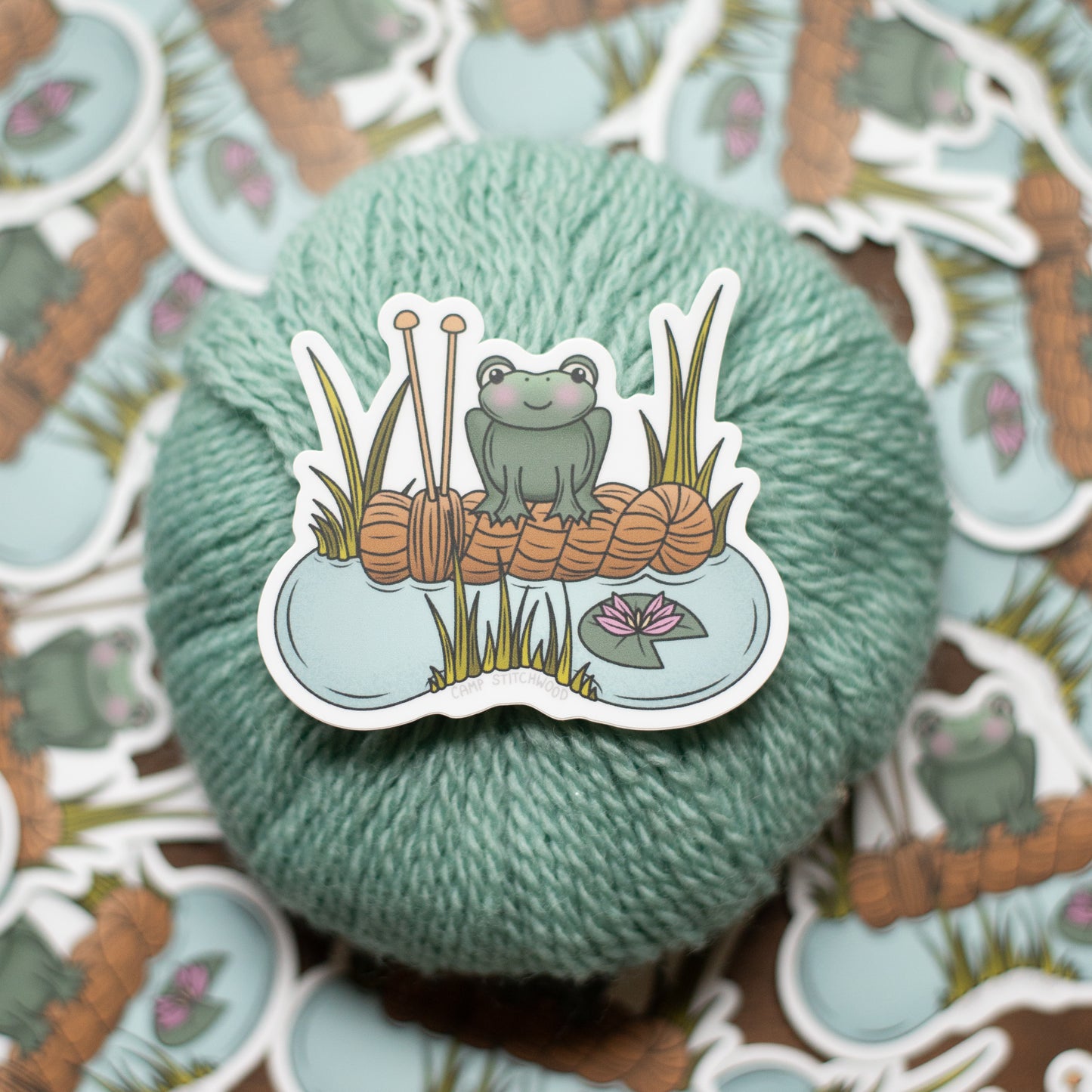 Yarn ball with a sticker of a frog and knitting needles on a patterned background