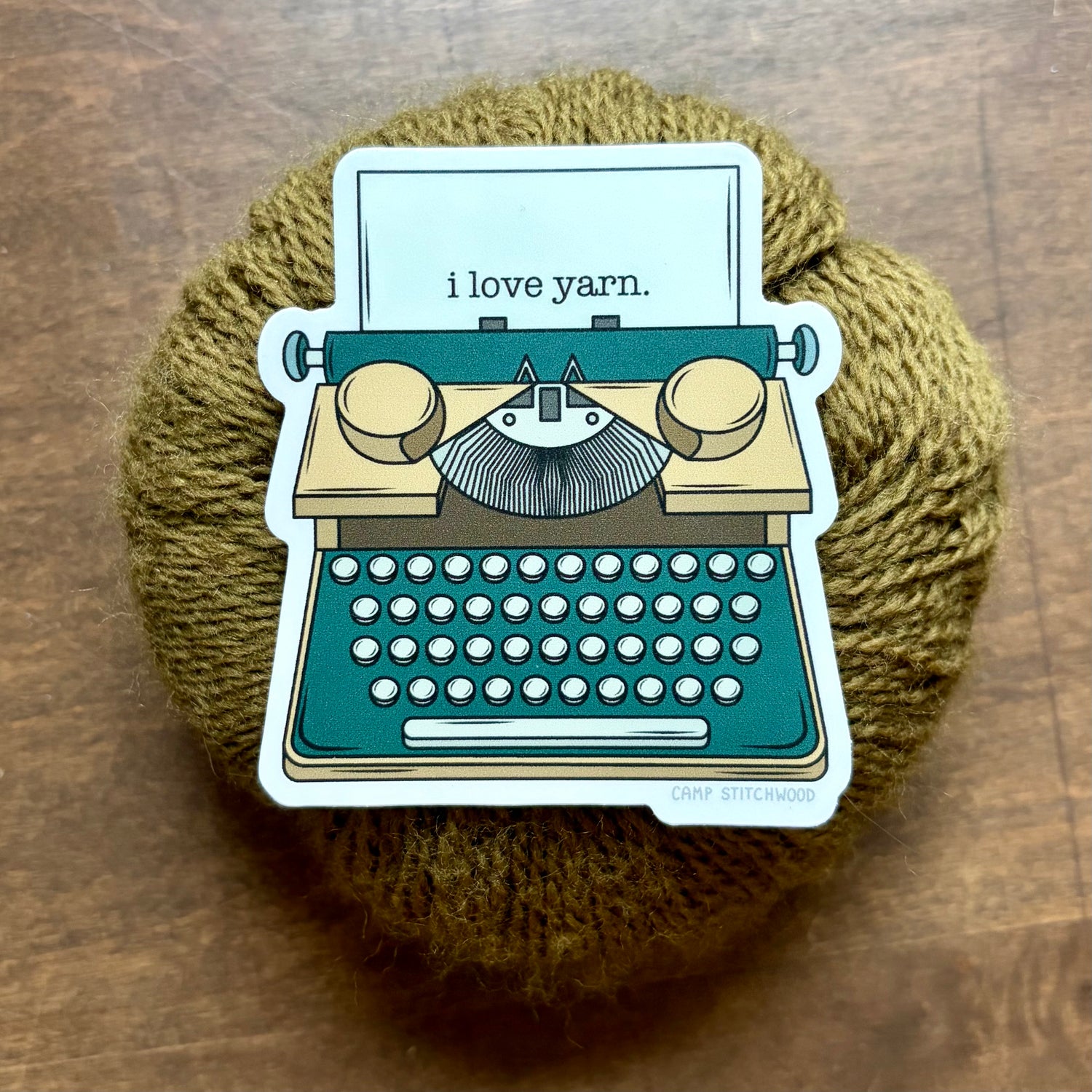 Sticker of a typewriter with 'I love yarn' text on a ball of yarn.