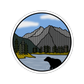Round sticker with a bear, mountain, and lake illustration on a white background