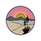 Round sticker with a desert landscape design featuring a sunset, mountains, and cacti.