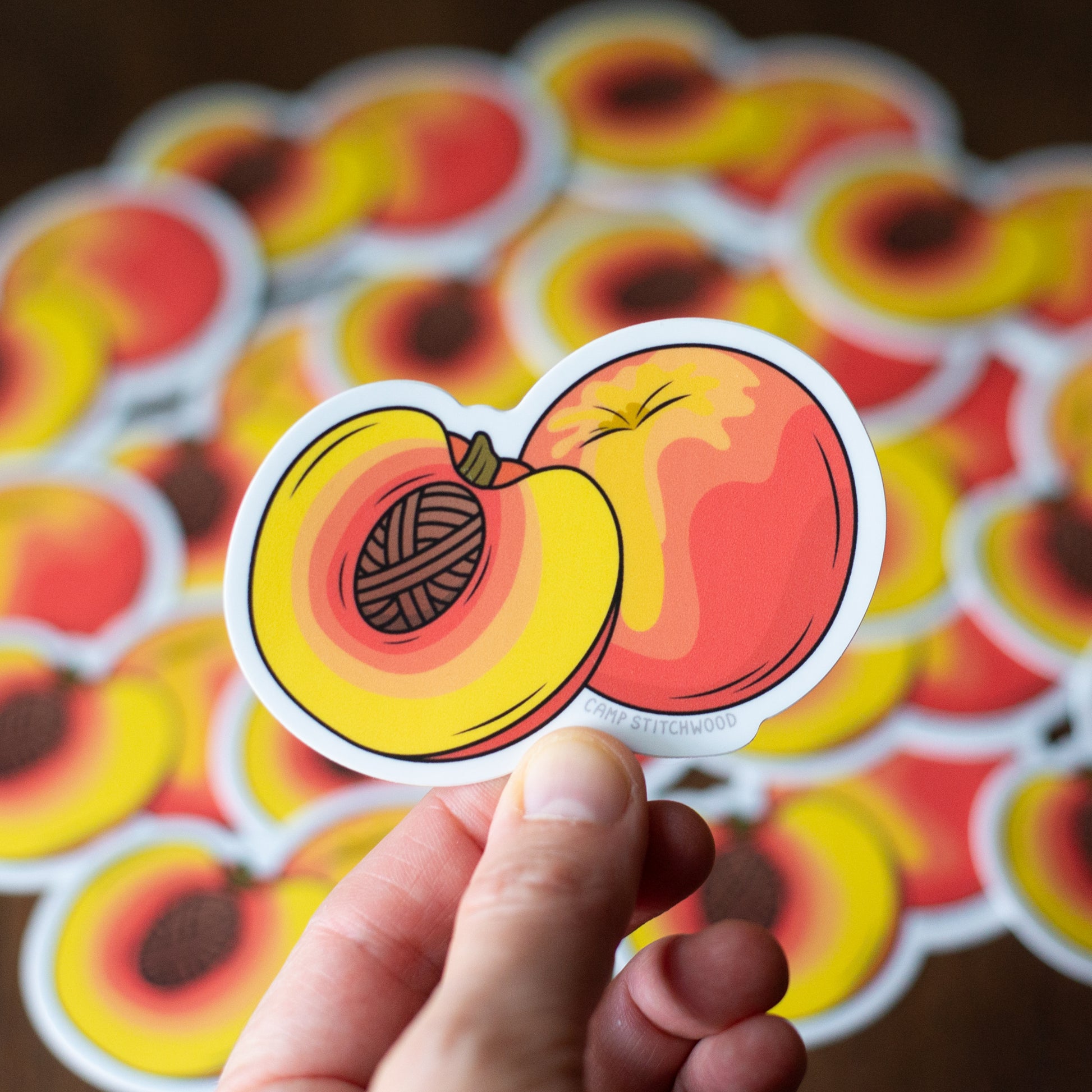Hand holding a sticker with a peach design featuring yarn inside, against a background of similar stickers.