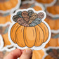 Sticker of a pumpkin with yarn on top held by a hand, with more stickers in the background.