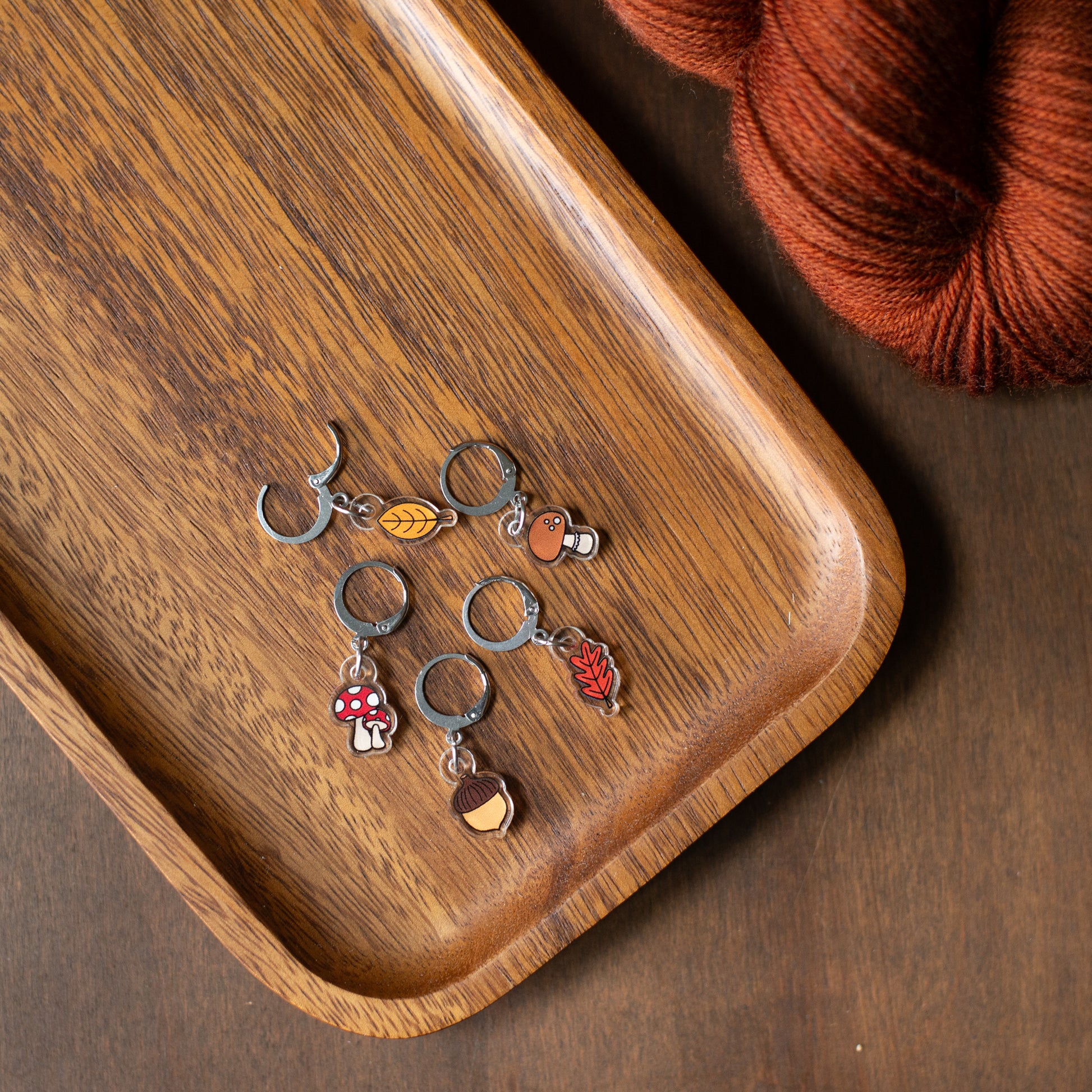 Wooden tray with fall forest stitch markers and yarn on a wooden surface