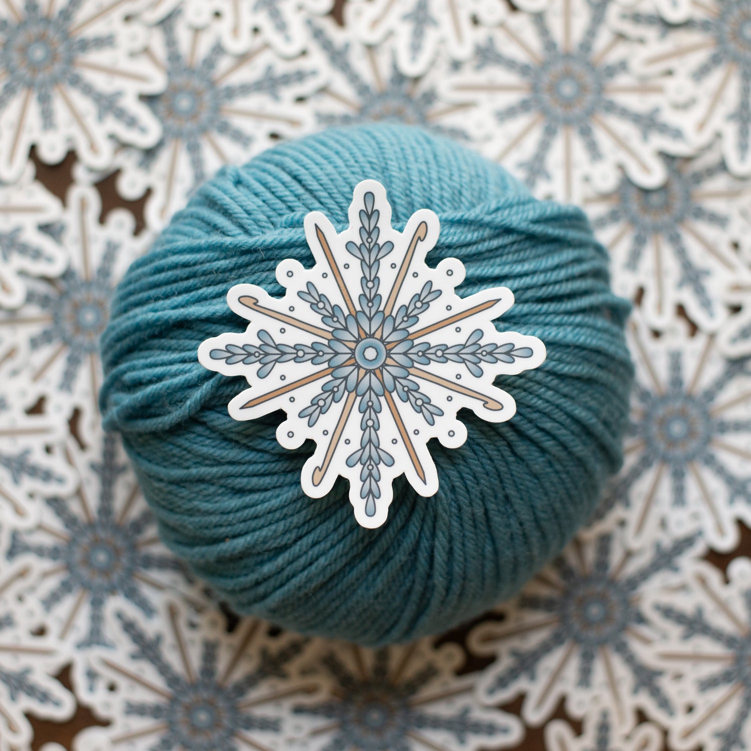Teal skein of yarn with a decorative snowflake sticker on a patterned background