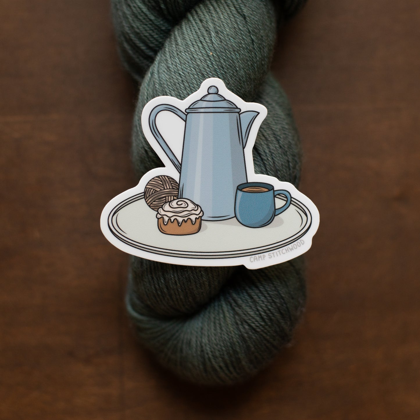 Sticker of a teapot, cup, and pastry on a skein of yarn.