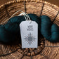 A skein of dark yarn with a 'Warm Wishes' tag on a woven basket background