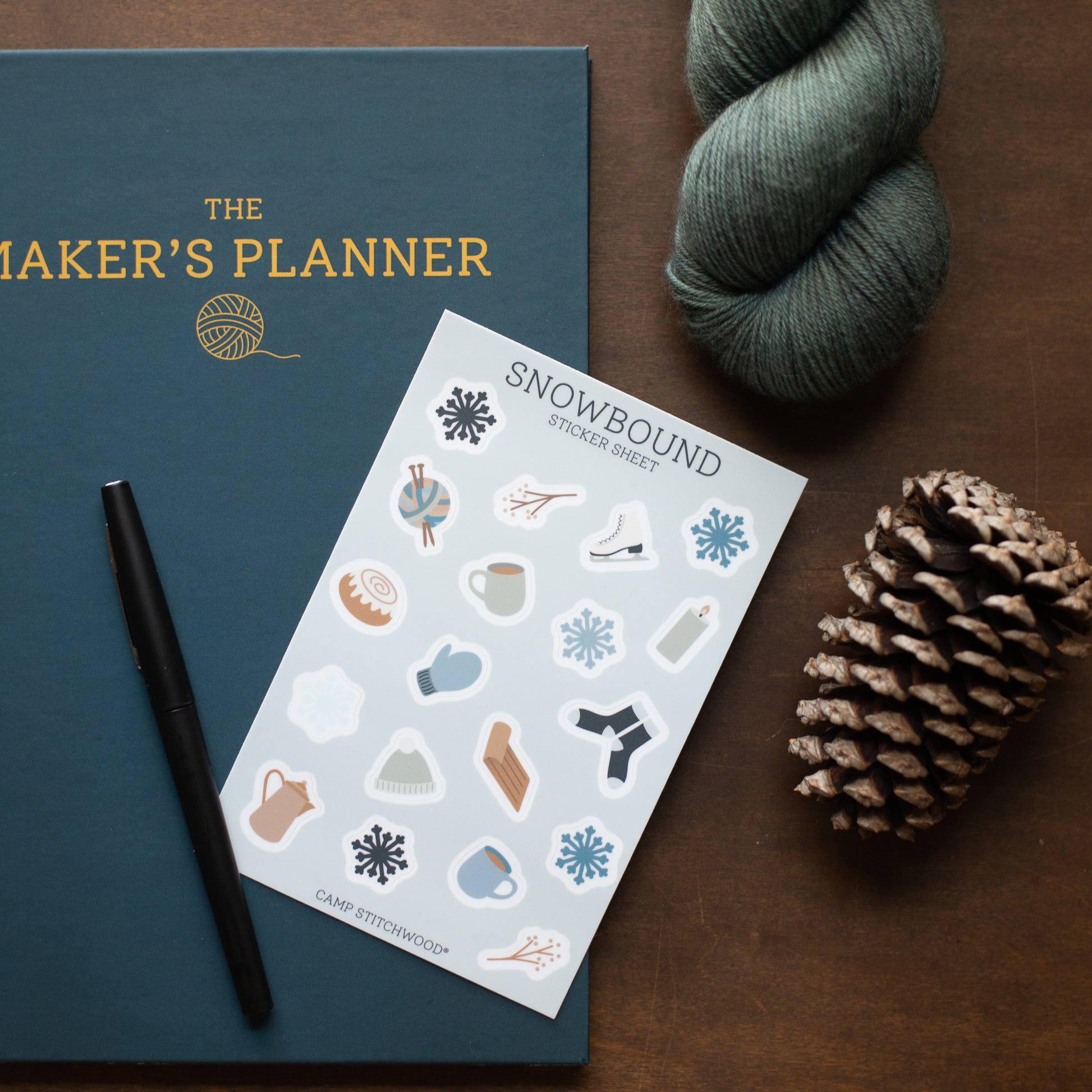 Maker's Planner with a sheet of 'Snowbound' stickers, pen, and yarn on a wooden surface
