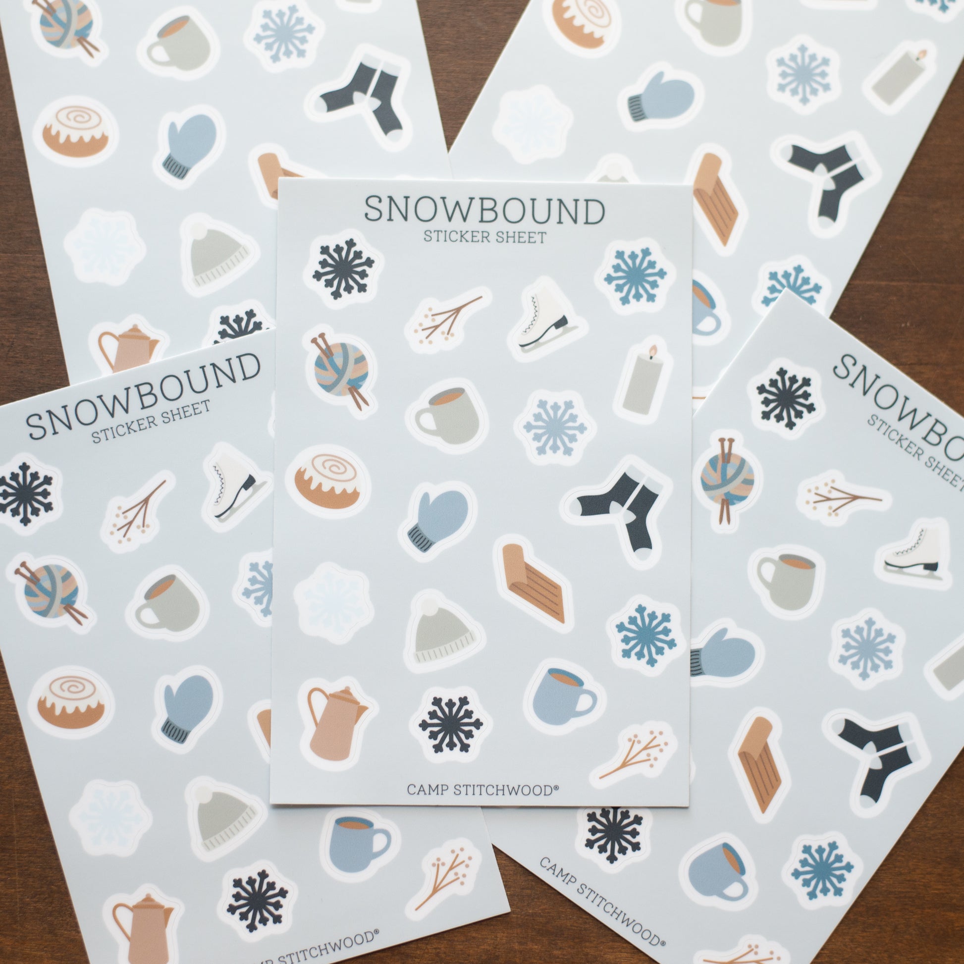 Five sheets of 'Snowbound' stickers with winter-themed illustrations on a wooden surface.