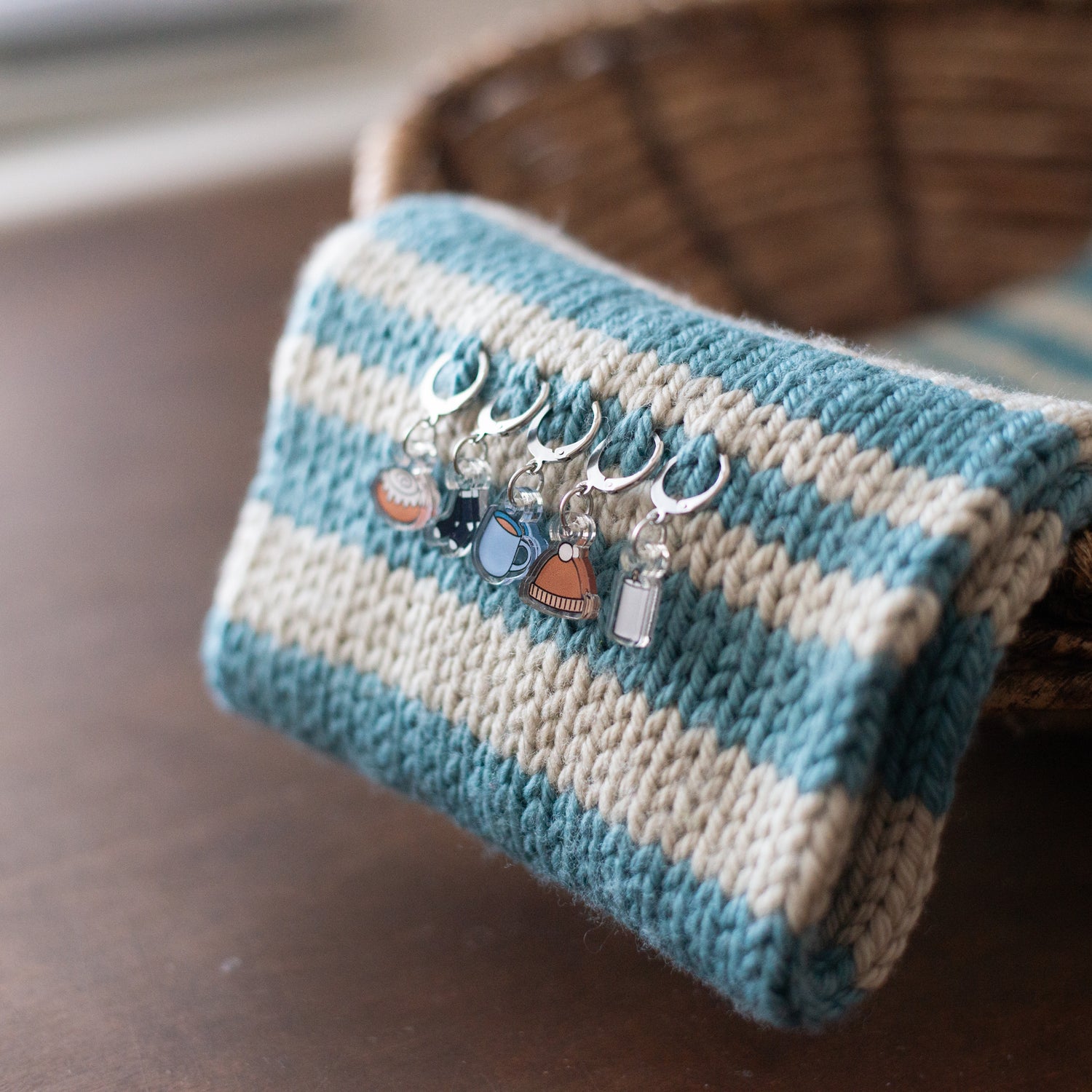 Knitted scarf with blue and white stripes and decorative stitch markers on a wooden surface.