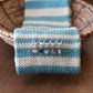 Knitted scarf with blue and white stripes and decorative stitch markers on a wooden surface.