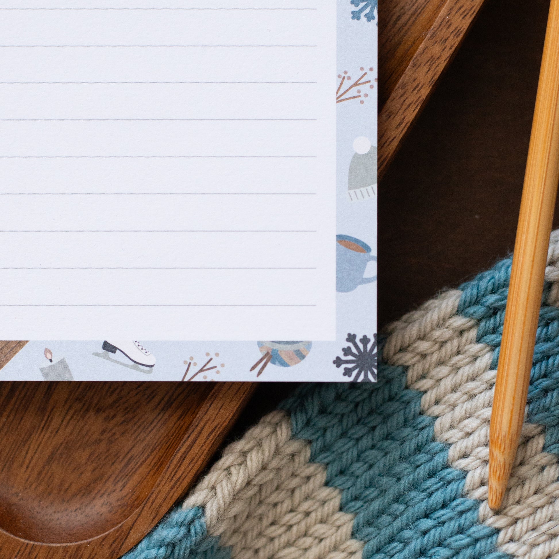 Notepad with a winter-themed design on a wooden surface with a textured scarf.