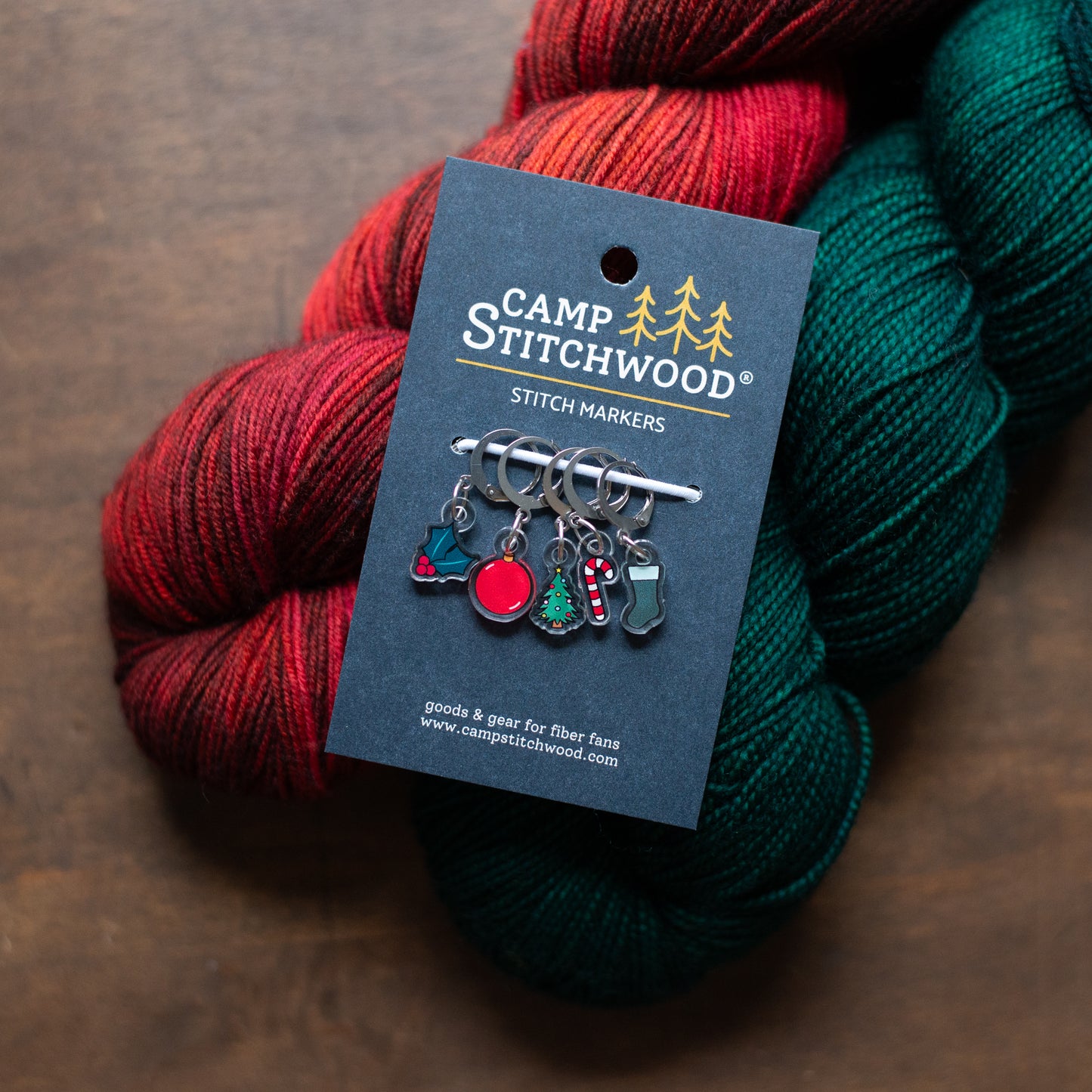 Camp Stitchwood stitch markers with red and green yarn on a brown background