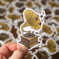 Sticker of a vintage gramophone held by a hand with a patterned background