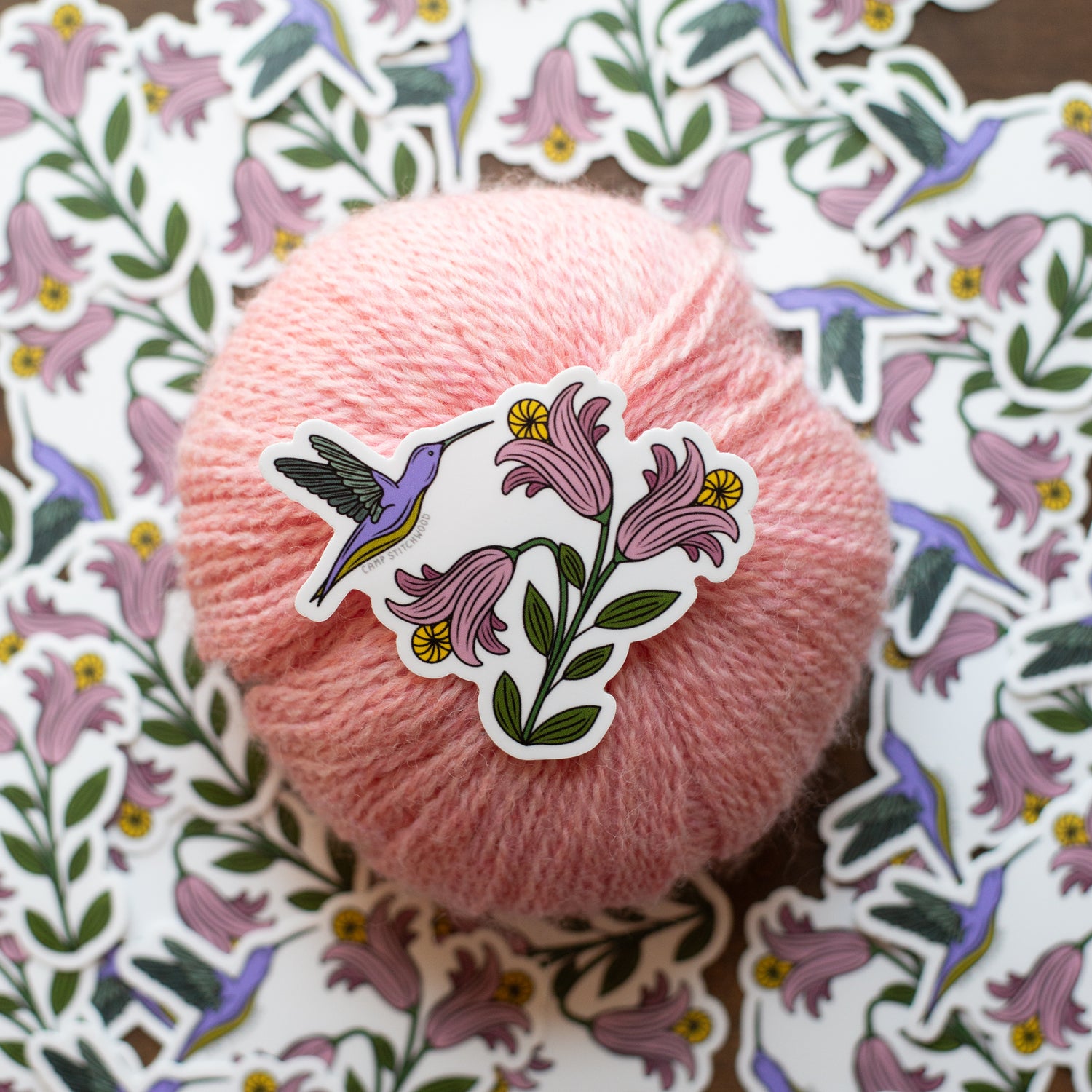 Pink yarn ball with a floral and hummingbird sticker on a decorative background