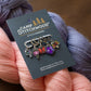 Camp Stitchwood stitch markers on a card with yarn in the background