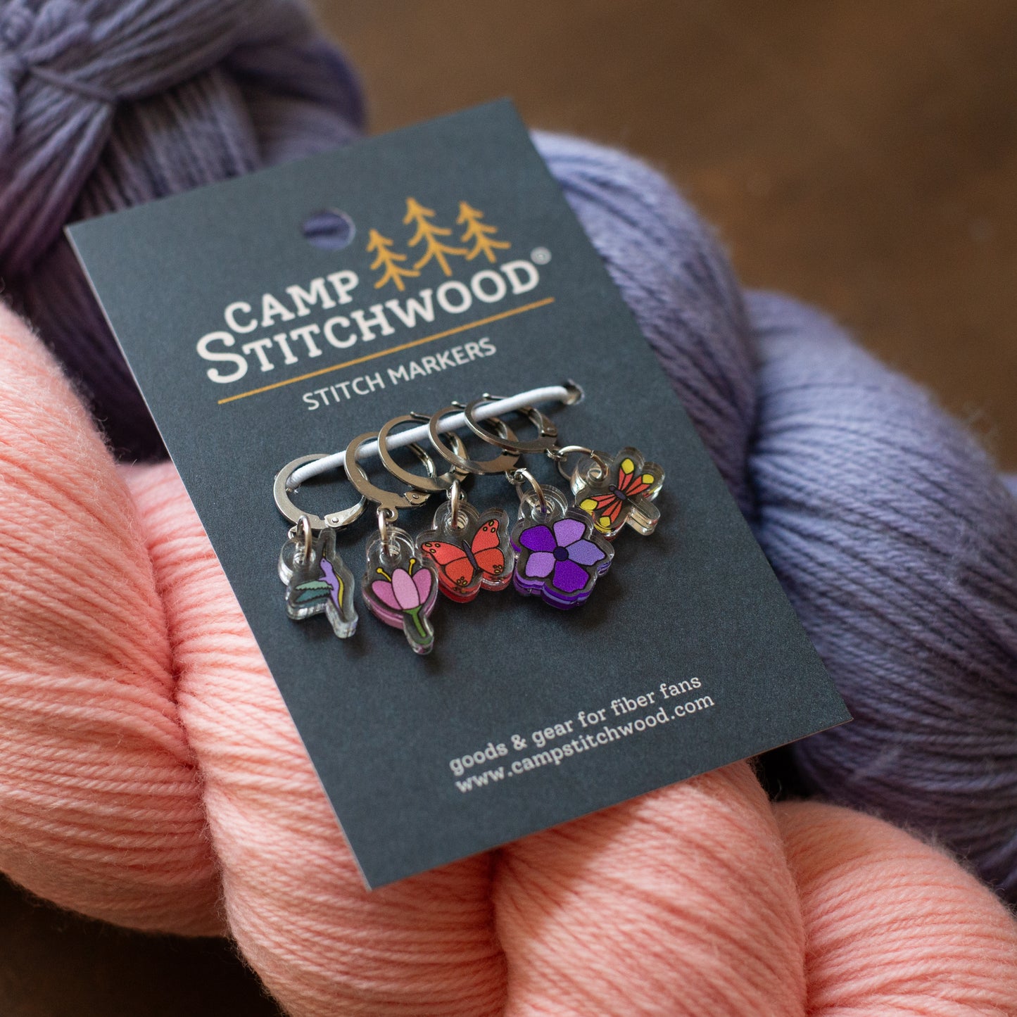 Camp Stitchwood stitch markers on a card with yarn in the background
