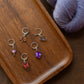 Set of colorful stitch markers charms on a wooden surface with purple yarn.