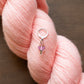 Pink yarn with a stitch marker featuring a pink flower on a brown background