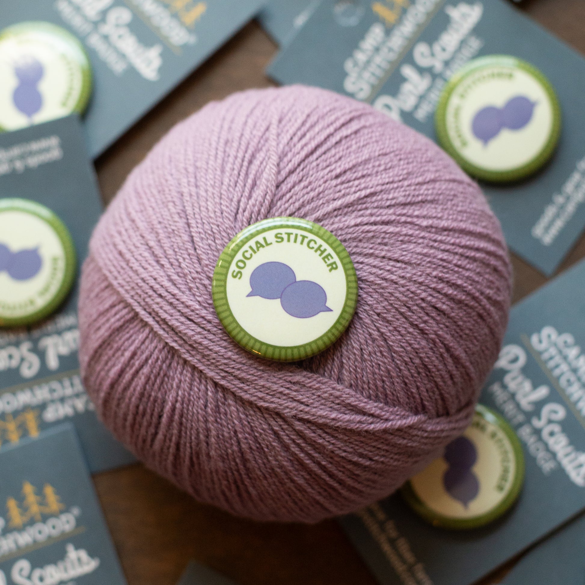 Ball of pink yarn with a 'Social Stitcher' label on a wooden surface with brochures.