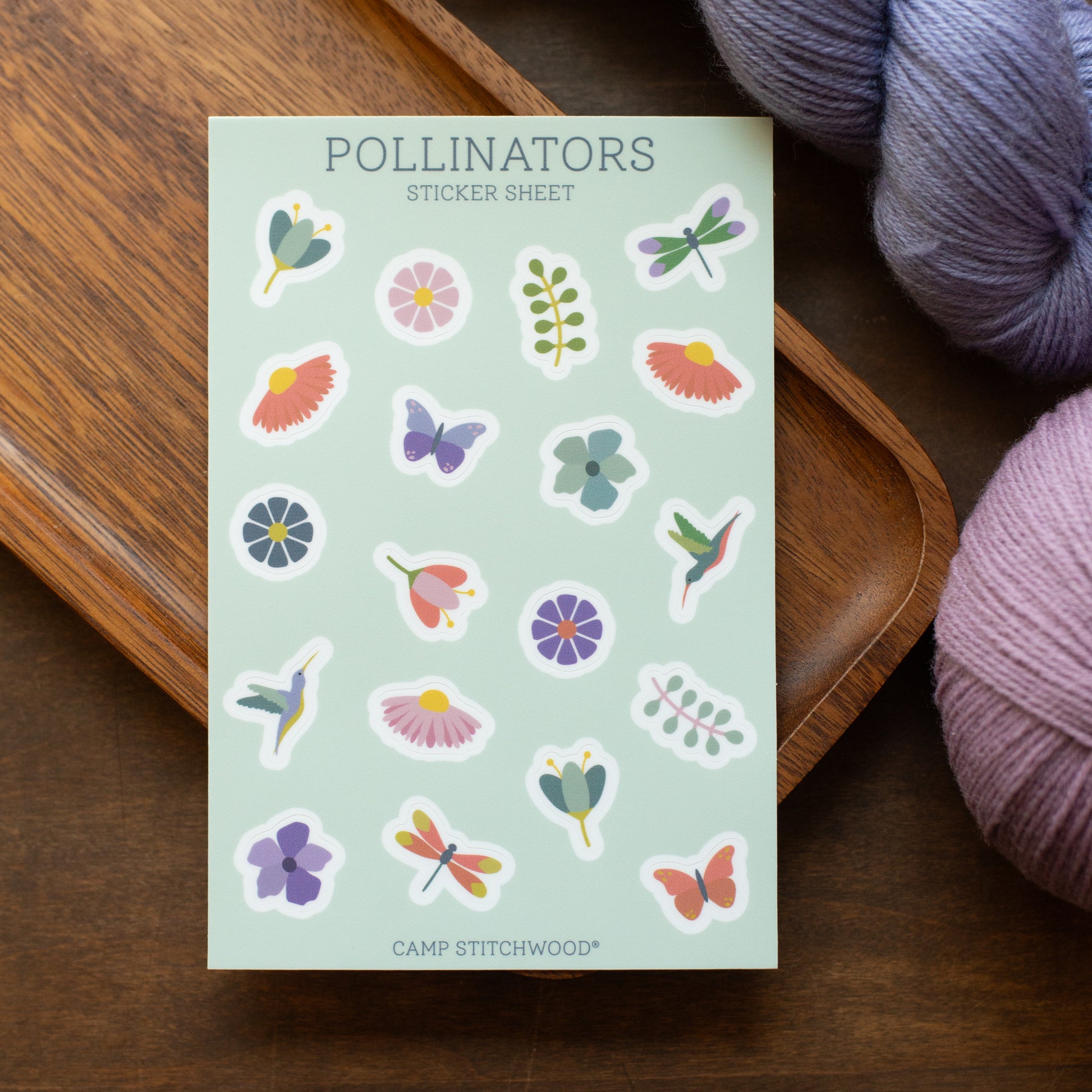 Sheet of colorful stickers with nature-themed designs on a wooden surface with yarn.