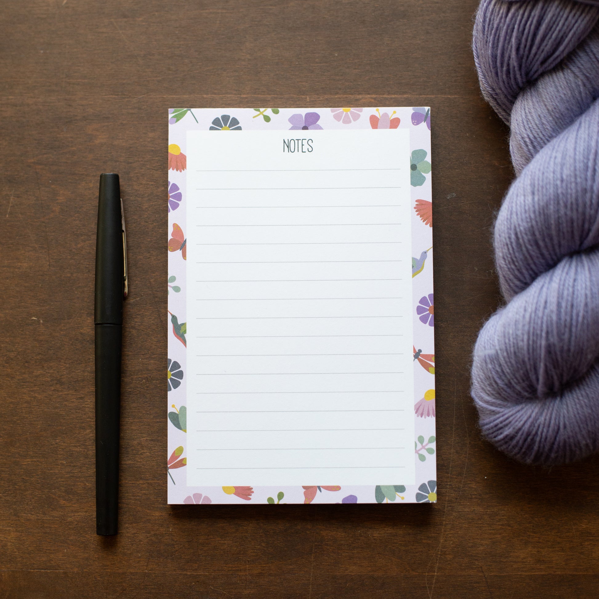 Notepad with floral pattern, pen, and yarn on a wooden surface