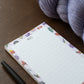 Floral notepad with 'NOTES' text on a wooden surface with yarn and pen.