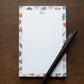 Floral-patterned notepad with 'NOTES' text and a pen on a wooden surface