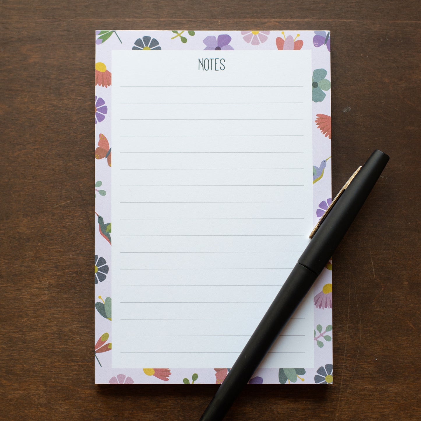 Floral-patterned notepad with 'NOTES' text and a pen on a wooden surface