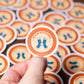 Hand holding a 'Sock Stitcher' badge with multiple badges in the background.