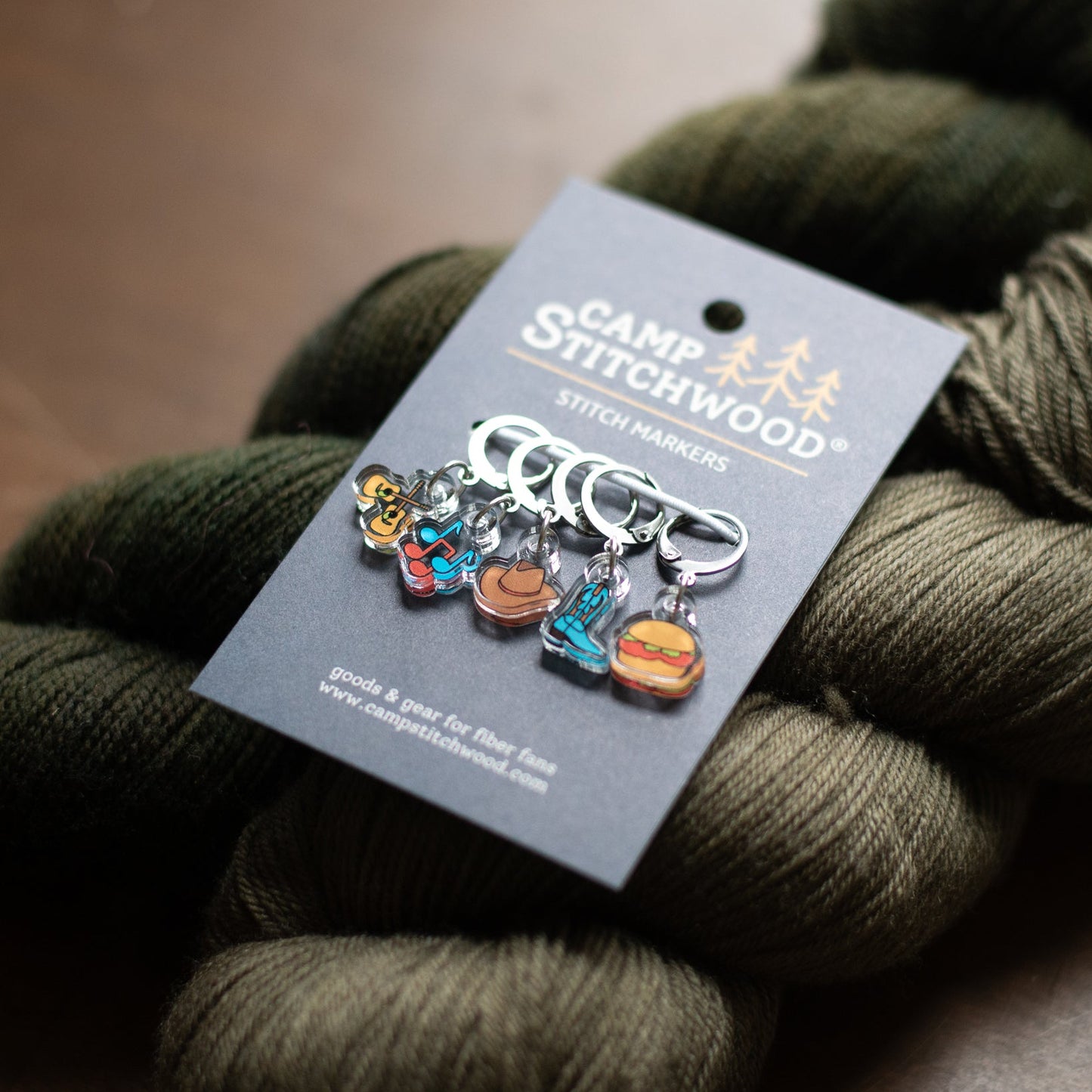 Set of colorful stitch markers on a Camp Stitchwood label with green yarn.