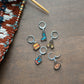 Set of colorful stitch markers on a wooden surface with knitting materials.