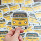 A die-cut vinyl sticker featuring a retro yellow Volkswagen Type I bus filled with colorful knitted yarn balls.