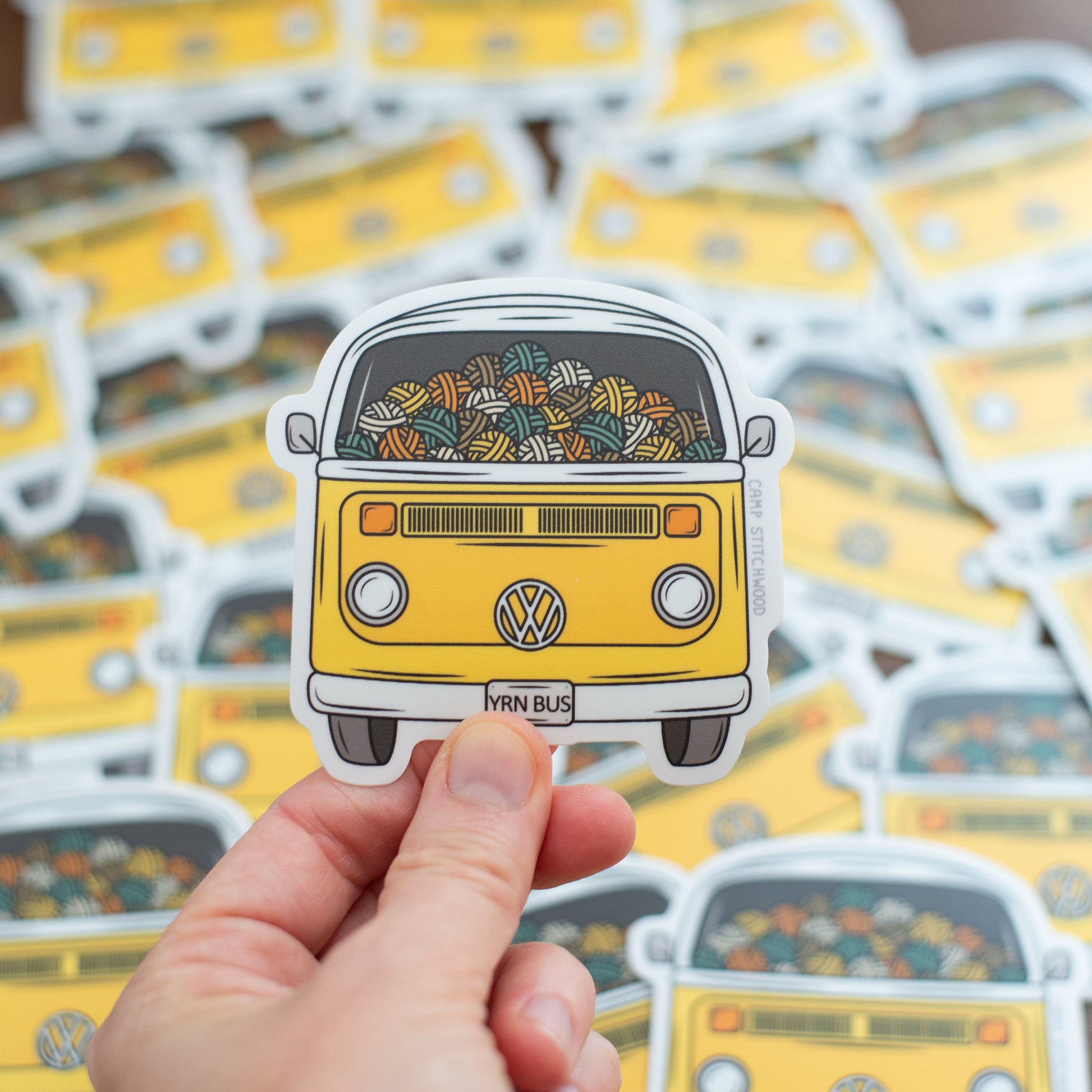 A die-cut vinyl sticker featuring a retro yellow Volkswagen Type I bus filled with colorful knitted yarn balls.