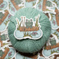 Yarn ball with a sticker of a frog and knitting needles on a patterned background