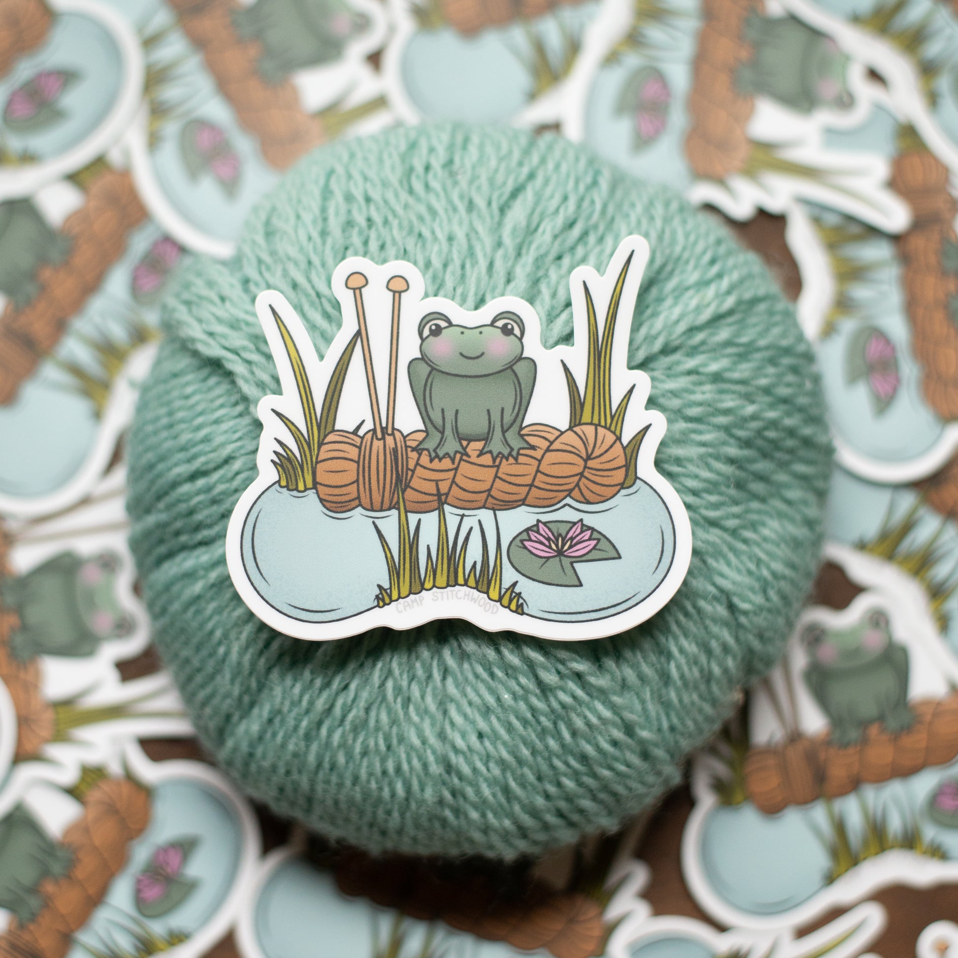 Yarn ball with a sticker of a frog and knitting needles on a patterned background