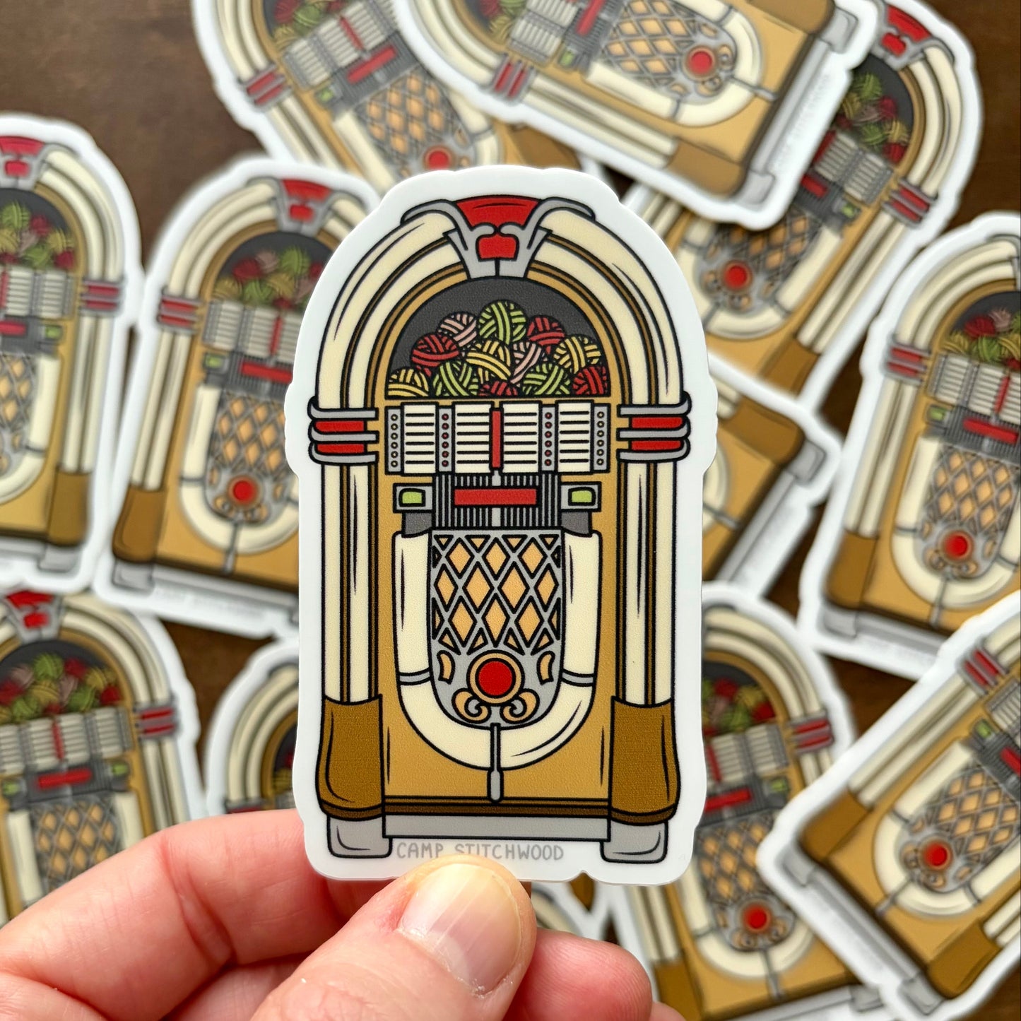 Hand holding a sticker of a vintage jukebox design with more stickers in the background.