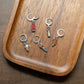 Five stitch markers with small enamel ice cream and popsicle designs, arranged on a curved wooden tray.